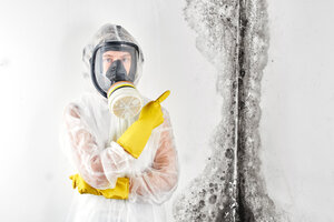 Person in safety suit and mask pointing at black mold on a wall